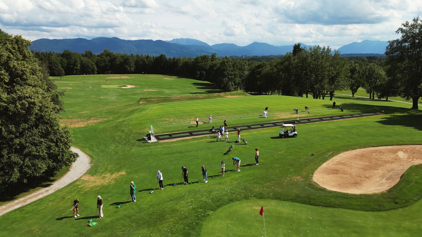 Driving Range mit Gästen, dahinter die Berge