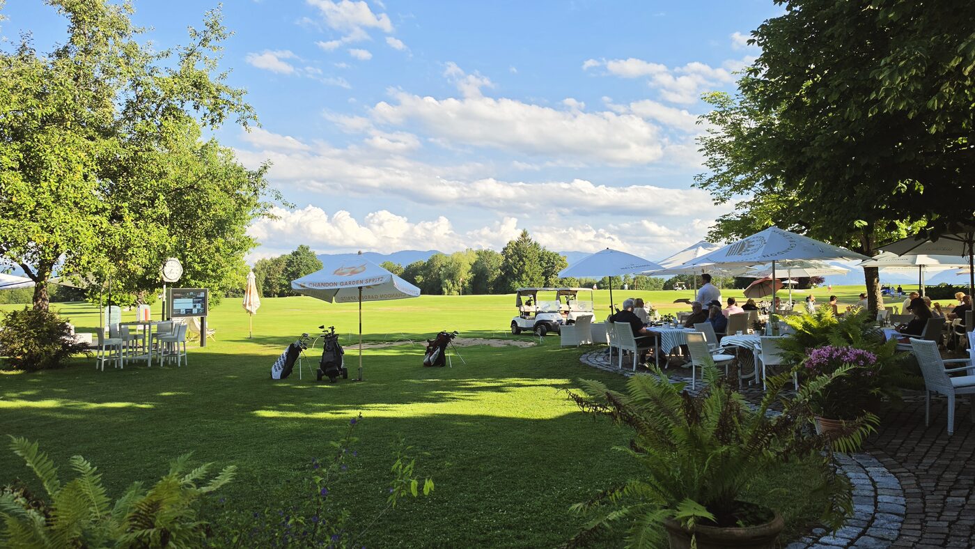 Terrasse mit Sonnenschirmen und Gästen, Blick auf die Anlage